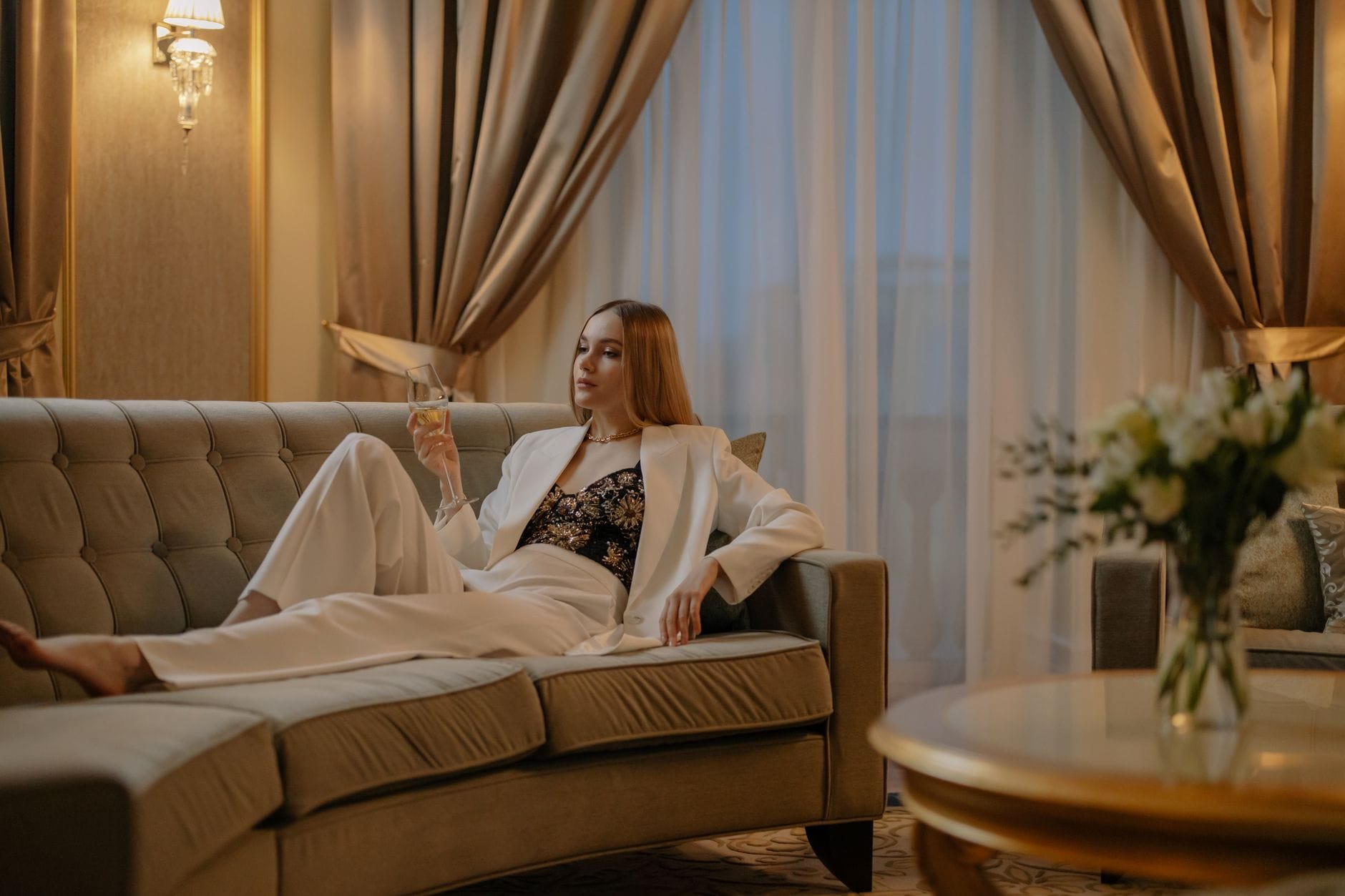 Elegancka kobieta w białym garniturze z kieliszkiem wina w luksusowym salonie